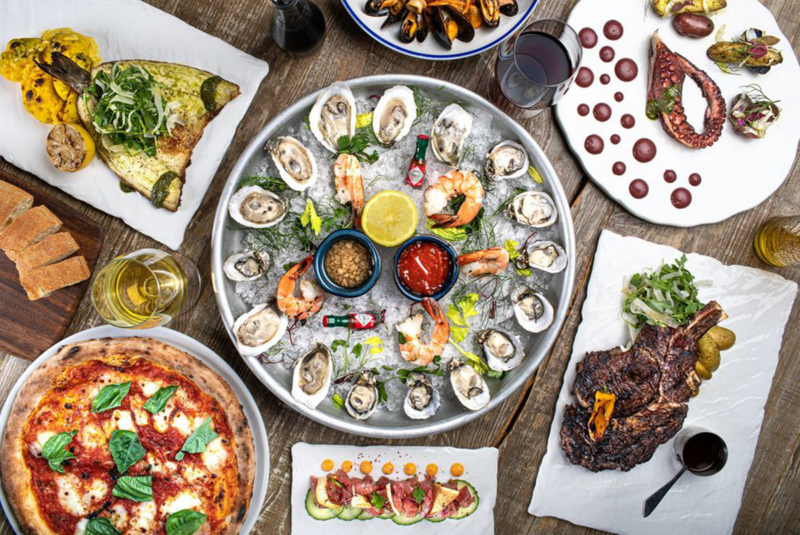 A vibrant overhead shot of an assorted Italian feast featuring fresh seafood, handmade pasta, and charcoal-grilled specialties.