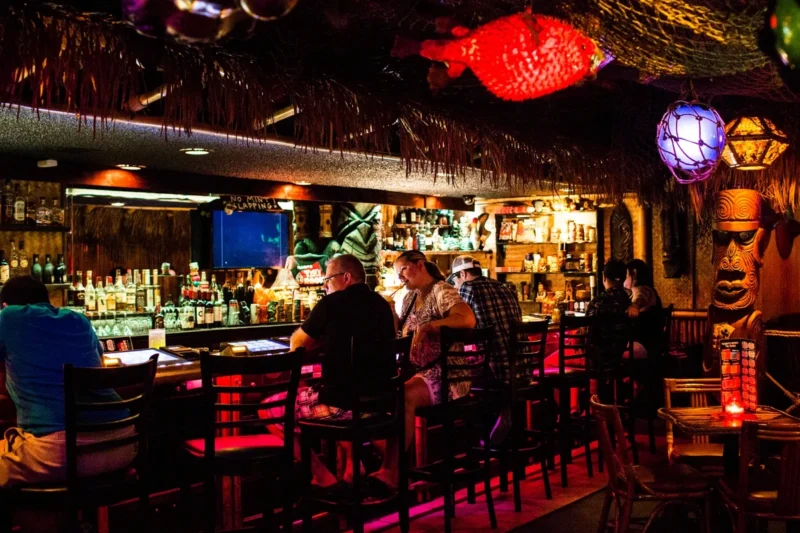 The dim, atmospheric interior of Frankie’s Tiki Room featuring carved wood totems and tropical decor.